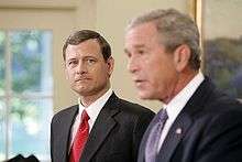 John Roberts appears in the background, while President Bush is 